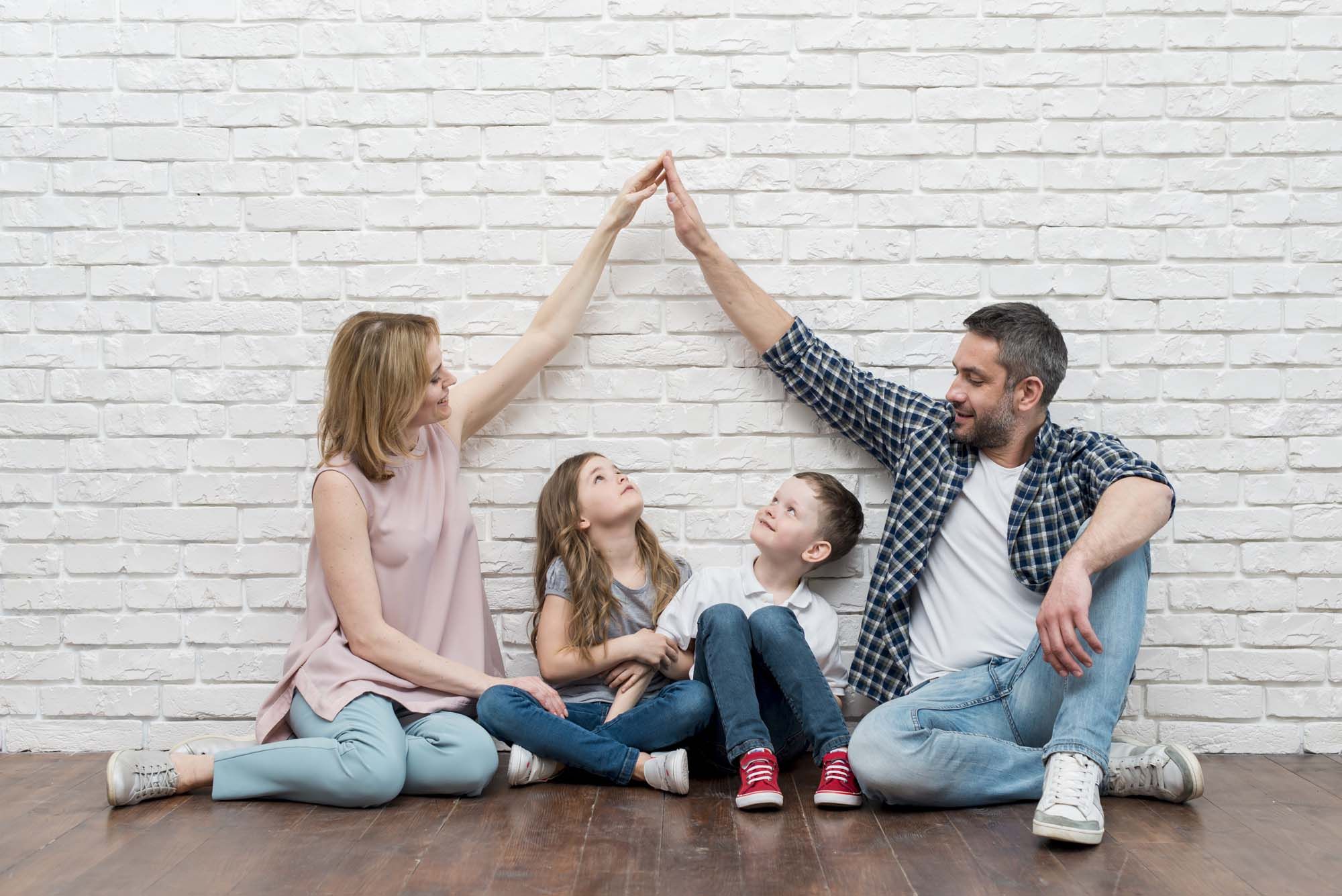 una famiglia seduta allegramente insieme, con il papà e la mamma che uniscono le mani a formare un tetto sopra la testa dei figli.